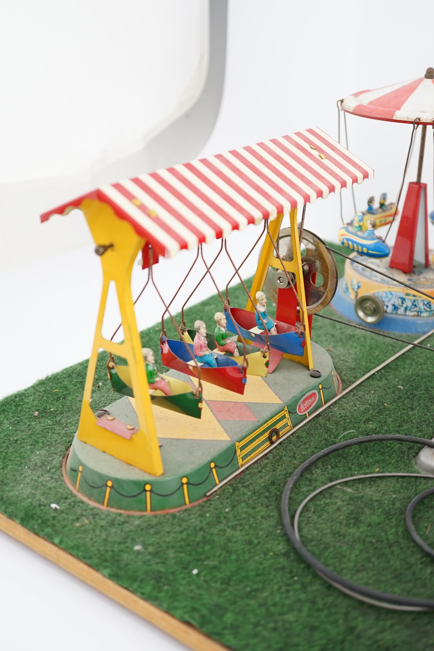 A Wilesco live steam fairground diorama, comprising a D430 pellet fired traction engine, powering a pulley and gear assembly, in turn running three tinplate fairground rides, mounted on a plywood sheet topped with grass